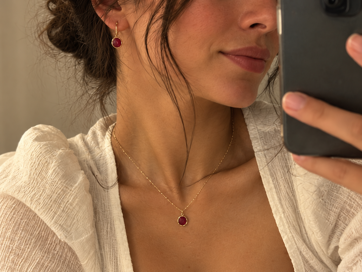 Mirror selfie of a woman wearing a gold ruby pendant necklace and drop earrings